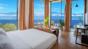 Habitación de hotel con una cama grande, zona de comedor y vista al mar.