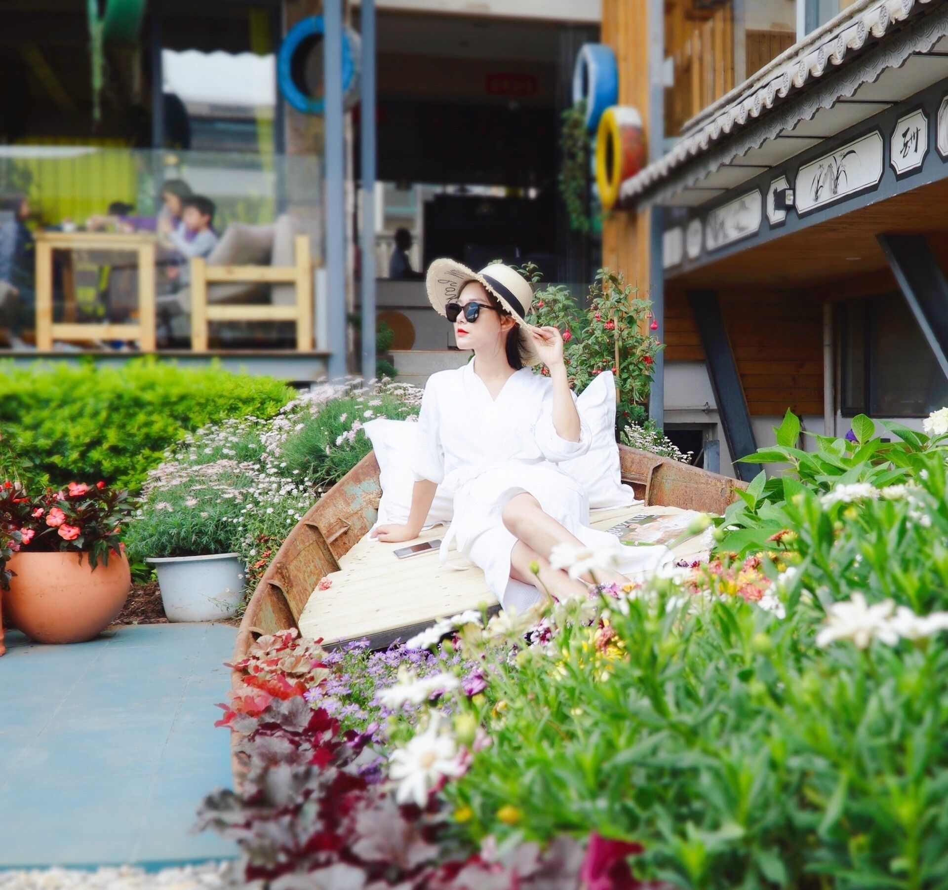 Una persona sentada en una terraza de madera rodeada de diversas flores y plantas.