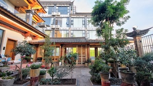 Un patio tradicional con plantas en macetas, un portón de madera y un edificio con tejado de baldosas.