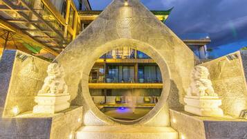 Un arco de piedra flanqueado por estatuas, que conduce a una zona de piscina con vistas a un edificio al fondo.