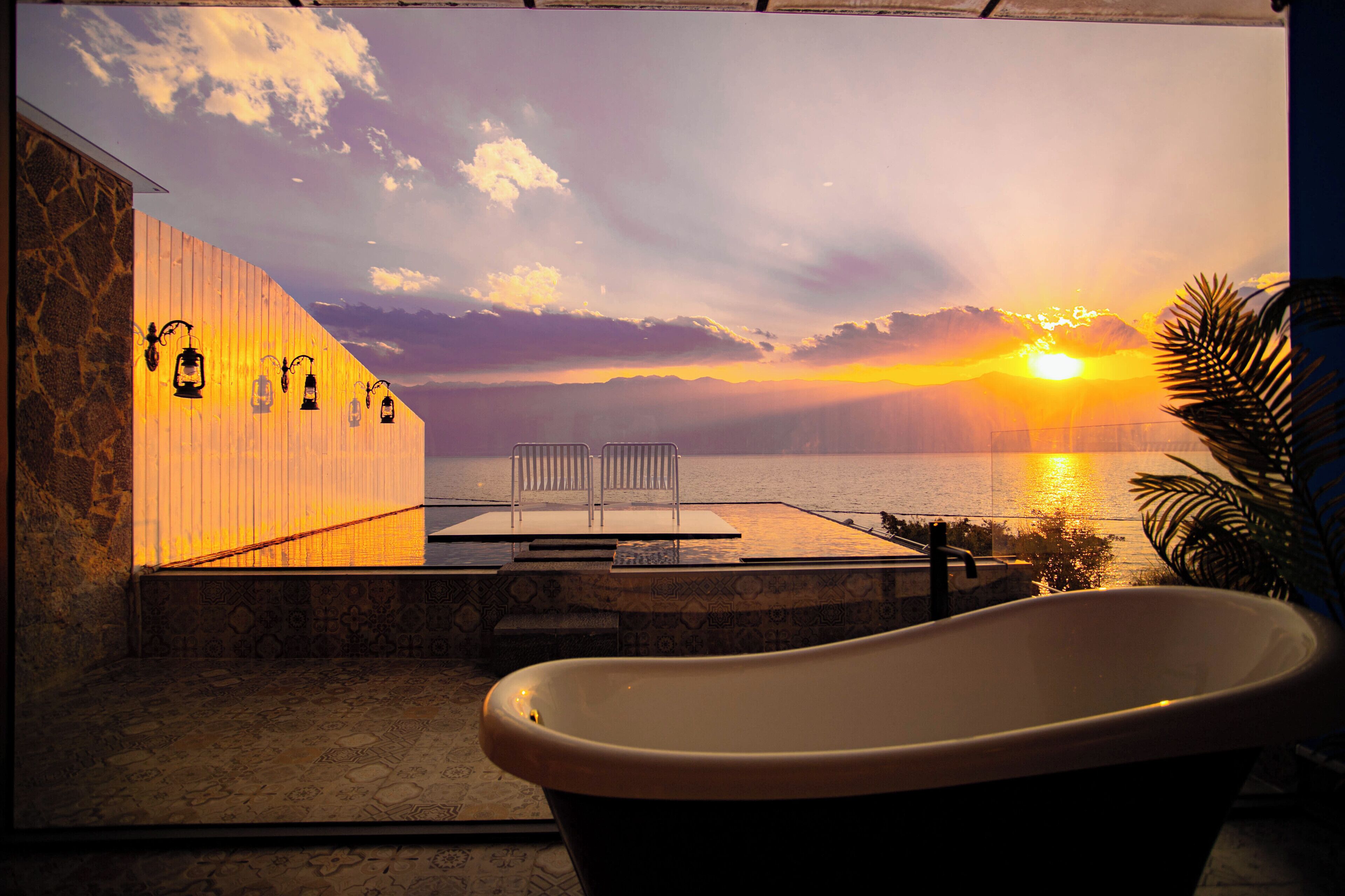 A bathtub in a room with a view of the sunset over the water.