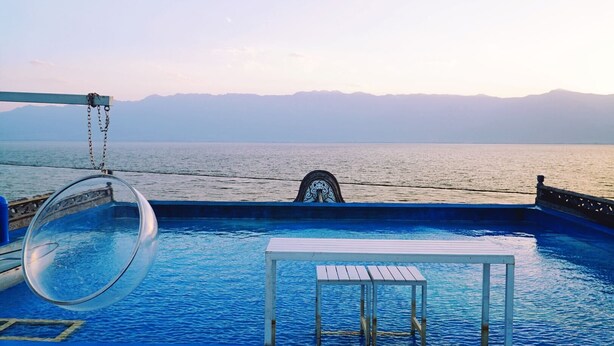 Zona de piscina con un tobogán de fondo de cristal, una mesa pequeña y vistas al mar y las montañas.