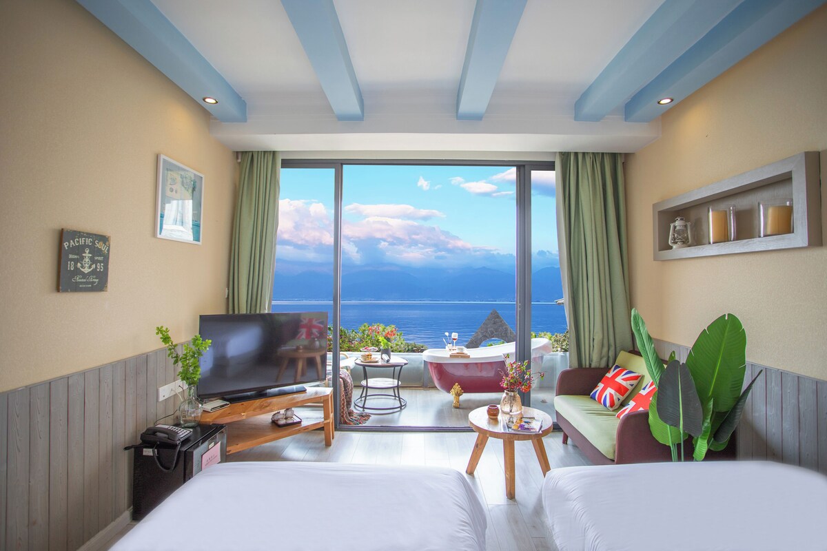 A hotel room with a television, a sofa, a small table, and a view of the sea.