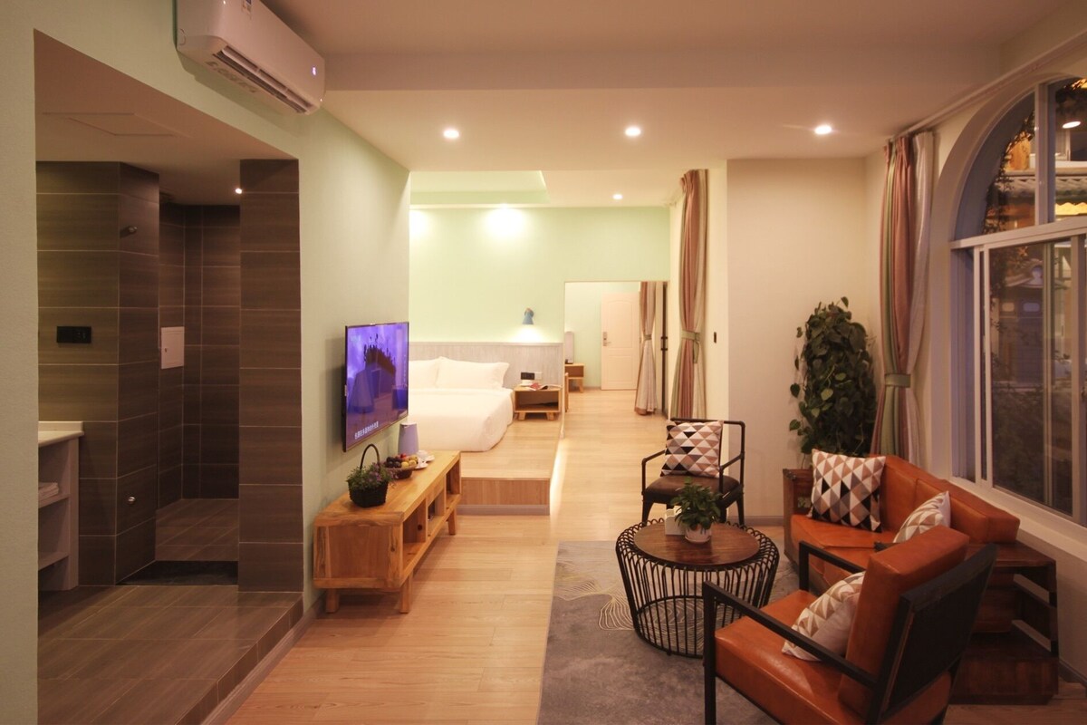 A modern hotel room with a bed, a TV, a wooden bench, a round coffee table, and a sofa.