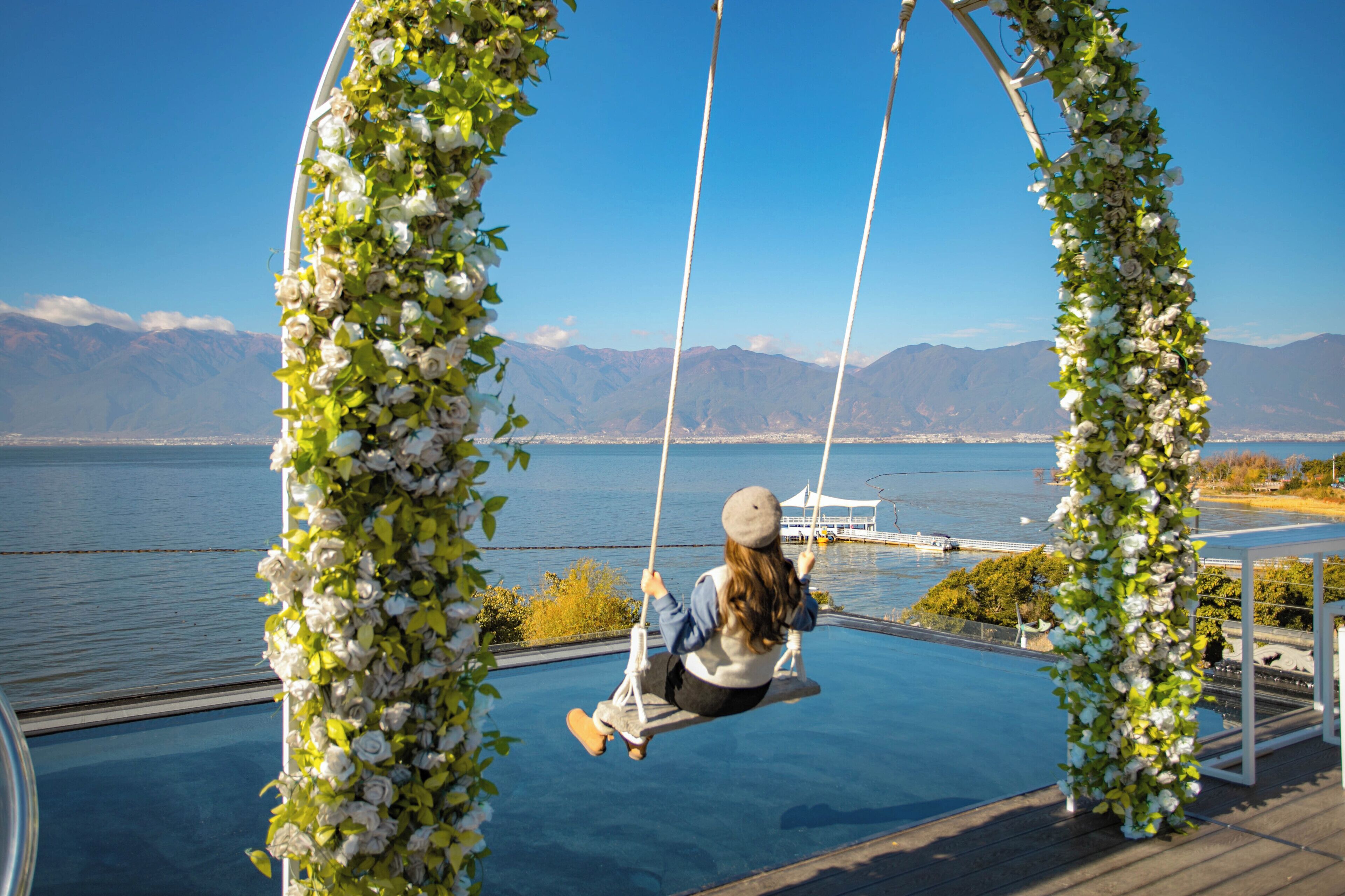 Una persona en una silla colgante con vista a un lago y montañas.