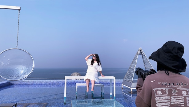 Una persona sentada en una mesa junto a una piscina, con vista despejada al océano.