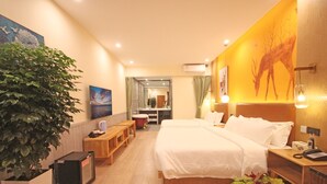 Habitación de hotel con cama, mesita de noche, lámpara y una planta grande en maceta.