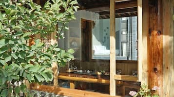 Un edificio tradicional de madera con base de piedra, escalones de madera que conducen a una puerta de madera, y una maceta con flores rosas en el frente.