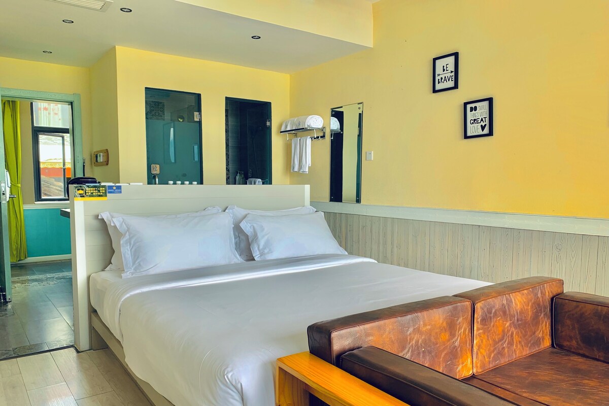 A hotel room with a bed, a wooden bench, a bathroom with a mirror, and a yellow wall with motivational quotes.