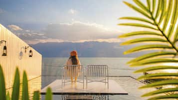 A person standing at a dock with a view of the sea and mountains in the distance.