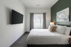 A hotel room with a bed, a flat-screen TV mounted on the wall, a window with curtains, and a painting on the wall. - Landing | Spectacular 2BD, Courtyard, Clubhouse (Dayton)