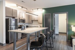 A modern kitchen with stainless steel appliances, a granite countertop, and a dining area with chairs.