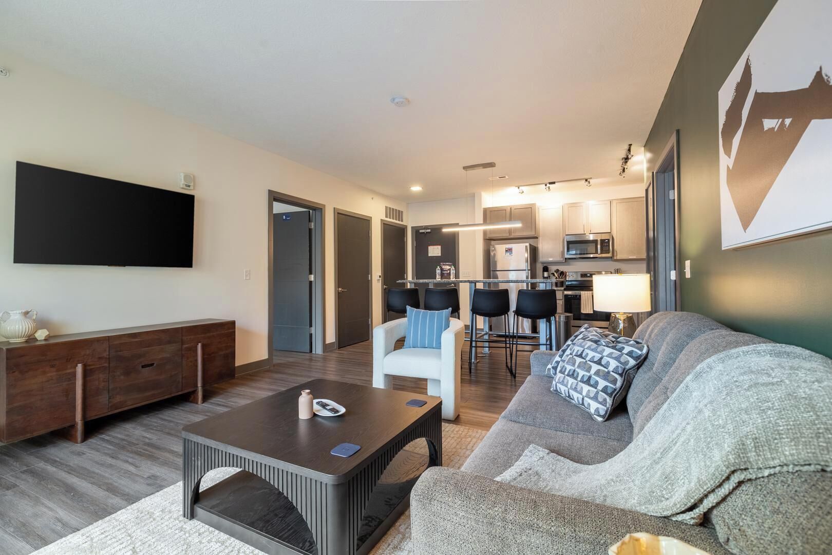 A modern living room with a flat-screen TV, a sofa, a coffee table, and a kitchen in the background.