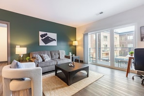 Una sala de estar moderna con un sofá gris, una mesa de centro y vistas a un balcón con mobiliario exterior.