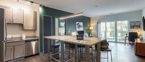 A modern kitchen with a granite countertop, stainless steel appliances, and a bar area with stools.