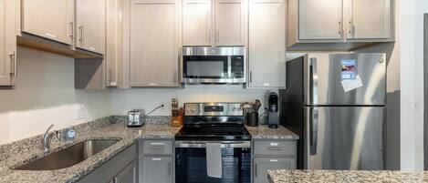 Una cocina moderna con electrodomésticos de acero inoxidable, encimeras de granito y armarios de colores claros.