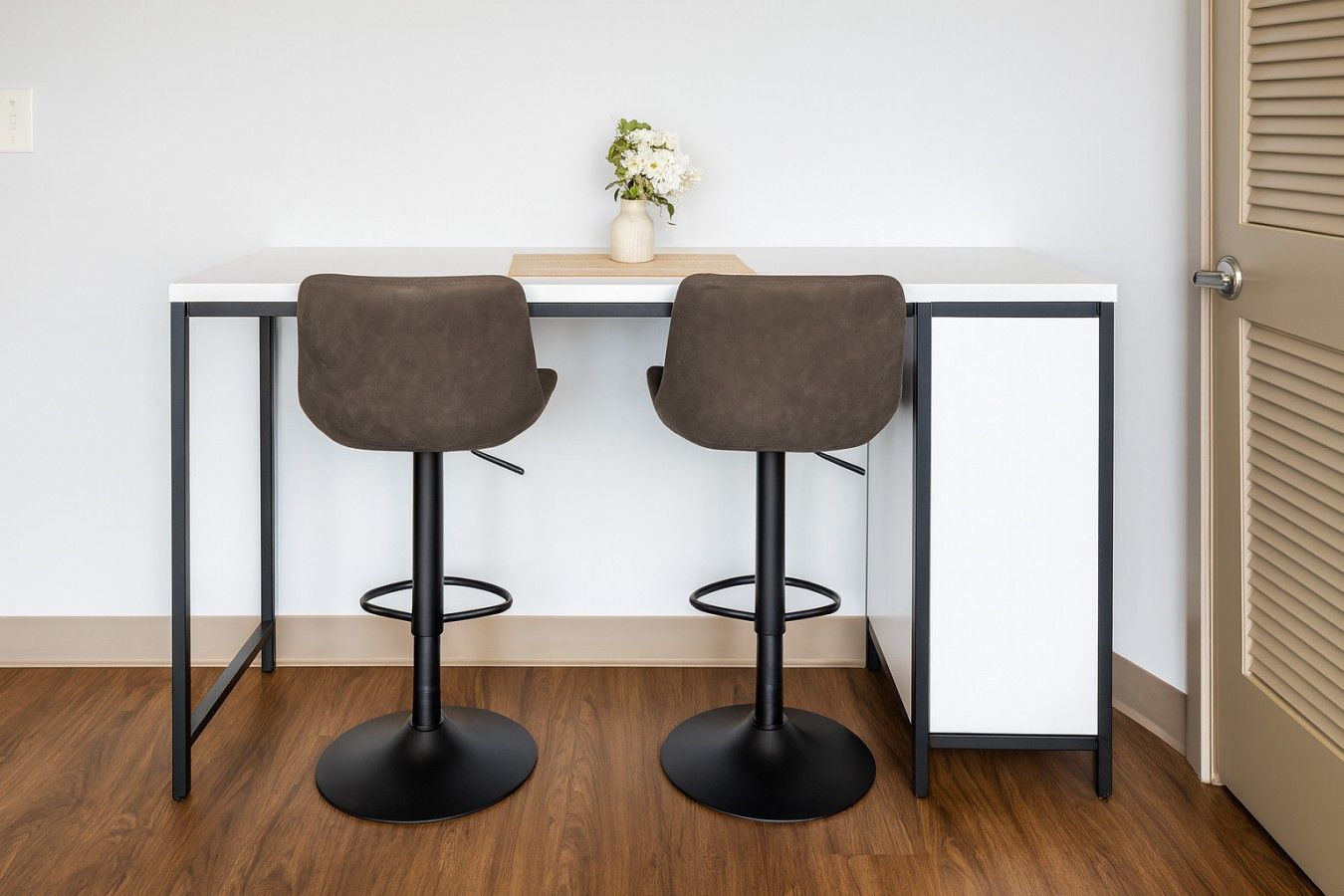 A modern room with a white desk and two bar stools.
