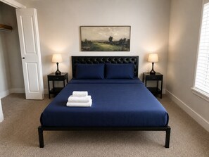 A bedroom with a bed, two bedside tables, a door, a painting on the wall, and a window. - Executive 3BR Downtown Birmingham W/ Game Table 9H (Birmingham)