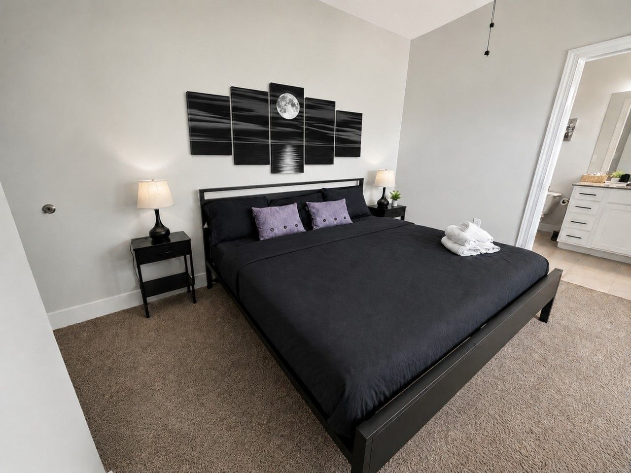 Une chambre à coucher avec un grand lit, deux tables de chevet, une œuvre d’art accrochée au mur et une porte donnant sur une autre pièce.