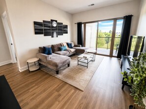 Ein modernes Wohnzimmer mit einer Sofagarnitur, einem Couchtisch und einem großen Fenster mit Balkon.