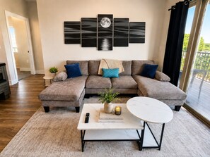A living room with a sectional sofa, a coffee table, and a wall-mounted artwork. - Executive 3BR Downtown Birmingham W/ Game Table 9H (Birmingham)
