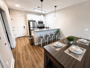 A modern kitchen with white cabinets, stainless steel appliances, and a bar area with stools. - Executive 3BR Downtown Birmingham W/ Game Table 9H (Birmingham)
