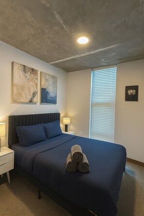 A bedroom with a bed, a nightstand, a lamp, and two wall-mounted artworks. - The Downtown Gem | Modern Luxe Escape 10H (Birmingham)