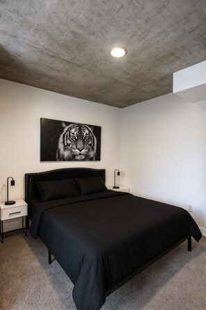 A bedroom with a large bed, a nightstand, a wall-mounted lamp, and a tiger print on the wall. - Trendy 3BR/3BA City Apt– Pool+Ping Pong 5F (Birmingham)
