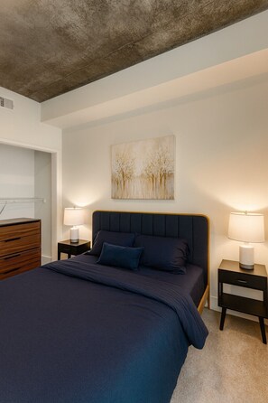 A bedroom with a large bed, two bedside tables, a dresser, and a painting on the wall. - Trendy 3BR/3BA City Apt– Pool+Ping Pong 5F (Birmingham)