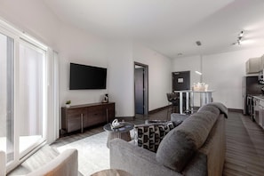 A modern living room with a sofa, a flat-screen TV, and a dining area with chairs and a table. - Landing | Spectacular 2BD, Courtyard, Clubhouse (Dayton)