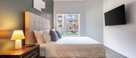 A modern bedroom with a bed, bedside table, lamp, and a TV on the wall.