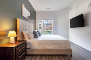A modern bedroom with a bed, bedside table, lamp, and a TV on the wall. - Landing | Spectacular 2BD, Courtyard, Clubhouse (Dayton)