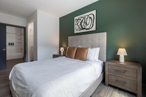 A hotel room with a large bed, two bedside tables with lamps, a wall-mounted abstract art piece, and a door leading to a bathroom. - Landing | Incredible 2BD, Clubhouse, Courtyard (Dayton)