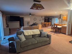 A living room with a gray sofa, a dining area with wooden chairs, a kitchen with wooden cabinets, and a ceiling fan. - Spacious 4-bedroom house in quaint Lakeview with AC. Beautiful private back deck (Lakeview)
