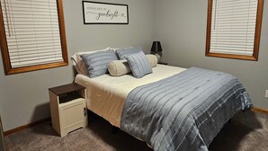 Quarto com cama, mesa de cabeceira, abajur e luminária na parede.