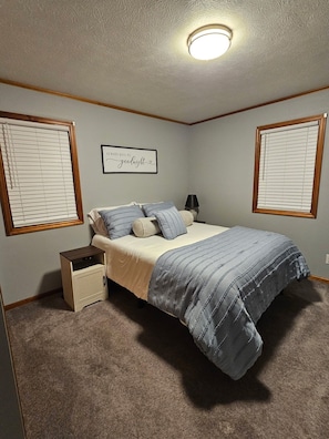A bedroom with a bed, a nightstand, a lamp, and a wall-mounted light fixture. - Spacious 4-bedroom house in quaint Lakeview with AC. Beautiful private back deck (Lakeview)