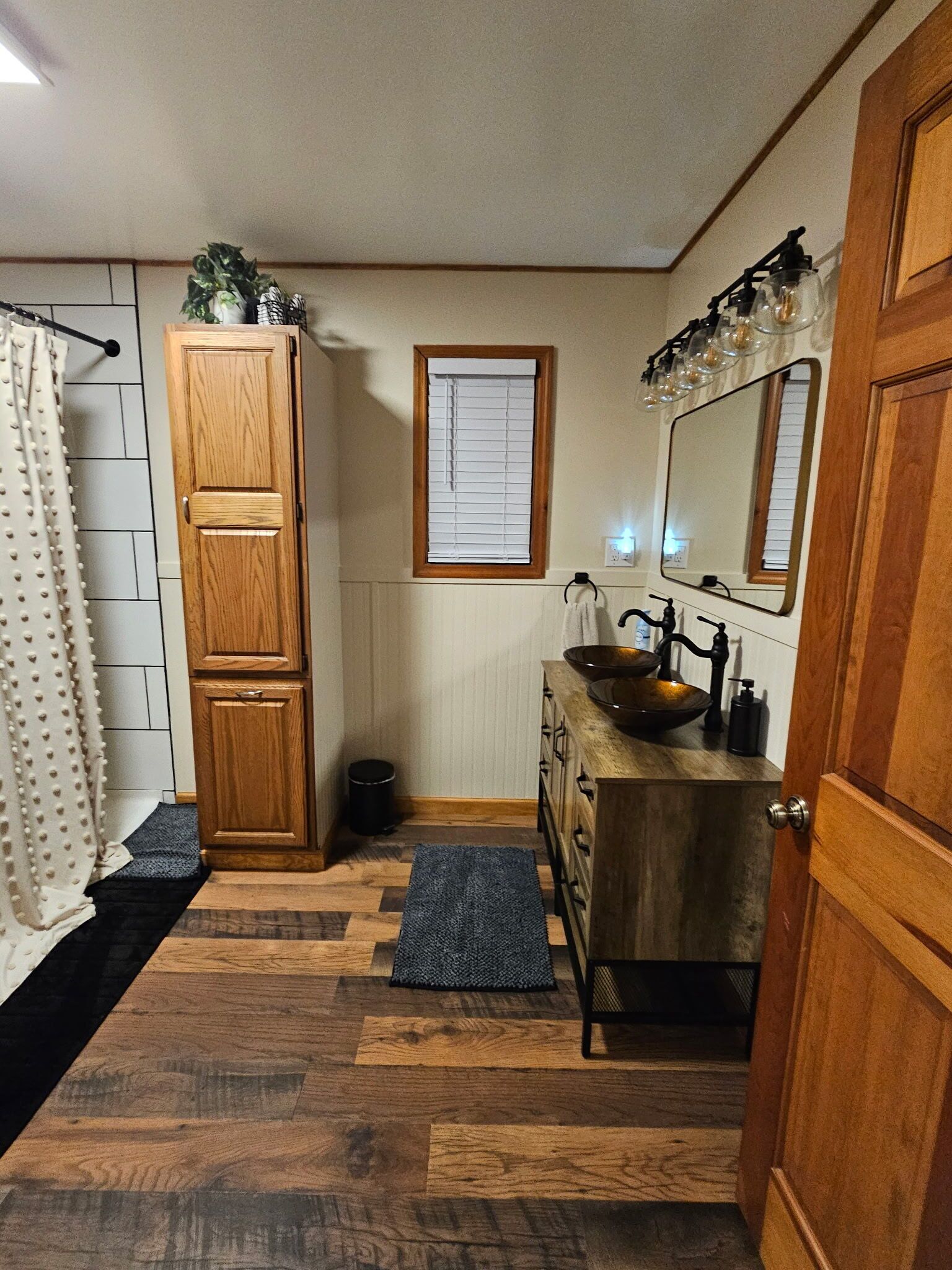 Une salle de bain avec un meuble en bois, un lavabo sur colonne, un miroir et un rideau de douche.