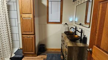 Une salle de bain avec un meuble en bois, un lavabo sur colonne, un miroir et un rideau de douche.
