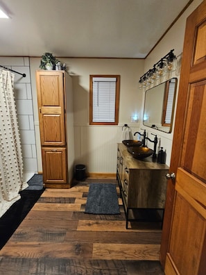A bathroom with a wooden cabinet, a sink with a vessel basin, a mirror, and a shower curtain. - Spacious 4-bedroom house in quaint Lakeview with AC. Beautiful private back deck (Lakeview)