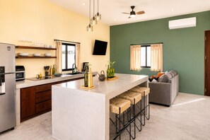 A modern kitchen with a central island, bar stools, a built-in oven, and a flat-screen TV. - Dreamy desert villa: luxe pool & ocean views (Todos Santos)