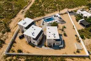 A modern residential complex with multiple buildings, a swimming pool, and a fenced perimeter. - Dreamy desert villa: luxe pool & ocean views (Todos Santos)