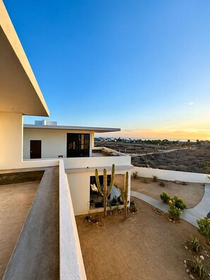 A modern house with a flat roof, a balcony, and a desert landscape in the background. - Dreamy desert villa: luxe pool & ocean views (Todos Santos)