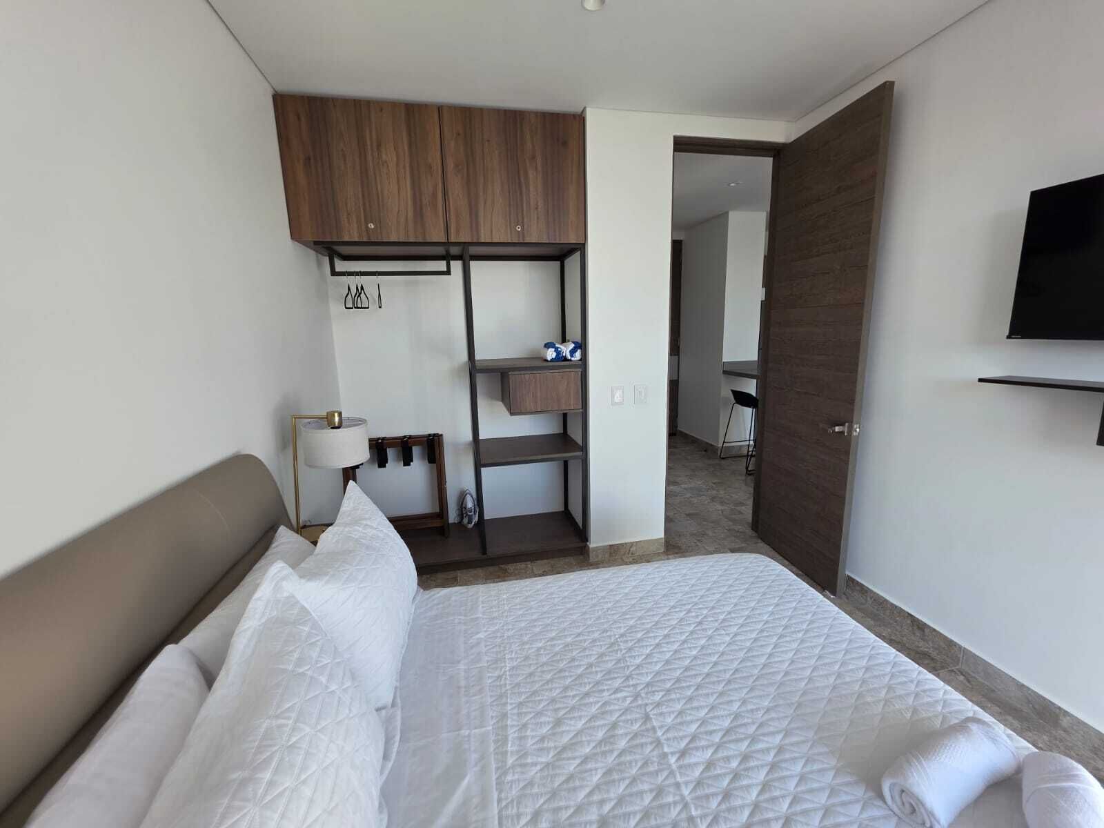 Ein Hotelzimmer mit Bett, Wandfernseher, Schreibtisch mit Stuhl und Kleiderschrank.