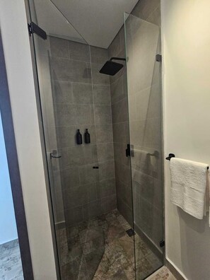 Un espace douche moderne avec des portes en verre, un mur de douche recouvert de carreaux et une serviette blanche suspendue à un crochet.