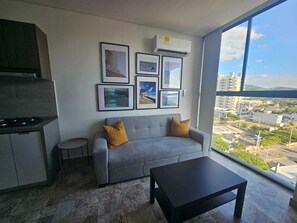 Ein modernes Wohnzimmer mit einem grauen Sofa, zwei Kissen, einem schwarzen Couchtisch und Blick auf die Stadt durch große Fenster.