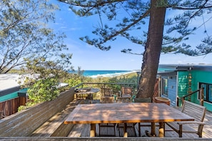 Une terrasse en bois avec une table et des chaises donnant sur une plage.