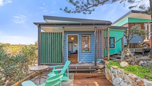 A modern house with a wooden deck, outdoor seating, and a stone wall. - The Headland Chalets - Cabin 3 (Point Lookout)