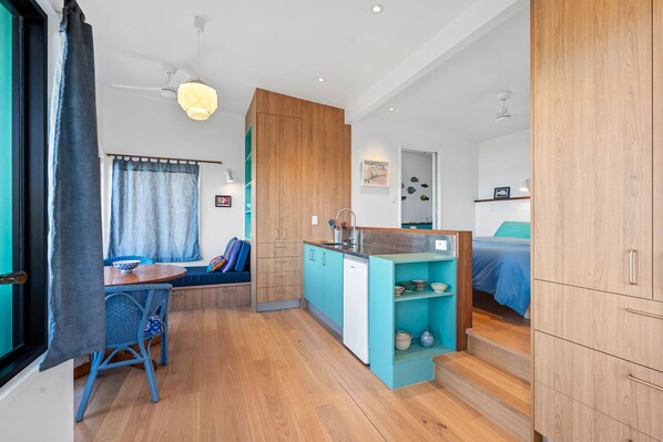 Un espacio habitable compacto con kitchenette, una zona de comedor con mesa y sillas, una sala de estar con sofá, y un dormitorio con cama.