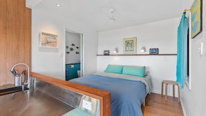 A modern bedroom with a bed, a wooden bench, a sink, and a bathroom visible through an open door. - The Headland Chalets - Cabin 3 (Point Lookout)