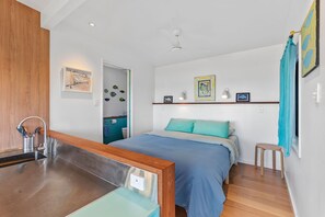 Une chambre à coucher moderne avec un lit, un banc en bois, un lavabo et une salle de bain visible à travers une porte ouverte.